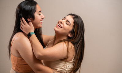 Couple of smiling young women hugging each other on pastel background.