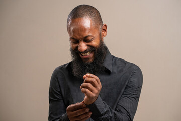 Bearded black man smiling, buttoning the cuff of his shirt on pastel background.