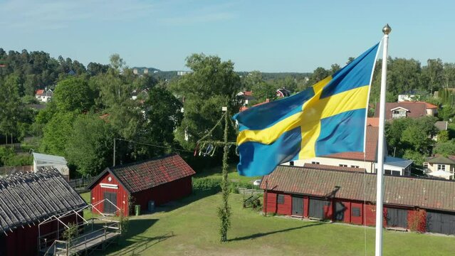 Swedish flag and midsummer may pole in background. Small red farm on countryside