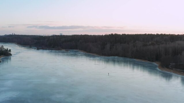 Single ice skater on frozen lake or river. Aerial shot winter at sunset Sweden