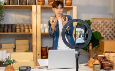 Selective focus mobile phone recording or streaming male business owner or entrepreneur on social media, selling products, making advertisement, marketing at home. Technology Concept.