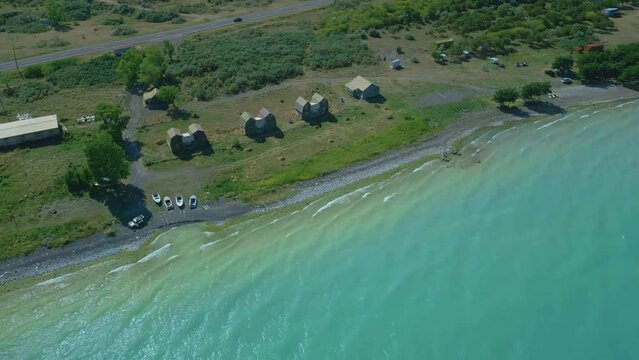 Aerial view of houses and boats, trees, beach big blue azure lake sea in clear sunny weather. Drone video, flying in an arc. Lake Sevan, Armenia.