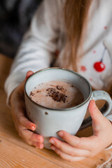 cute little girl in Santa hat and pajamas drinks cocoa with marshmallows in the kitchen at home on Christmas day