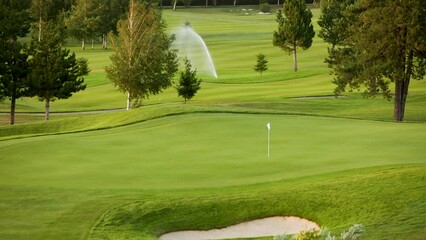 Automatic high-pressure water sprinkler at green golf course watering the grass.