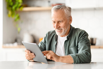 Fototapeta premium Happy Senior Man Using Digital Tablet While Relaxing At Table In Kitchen