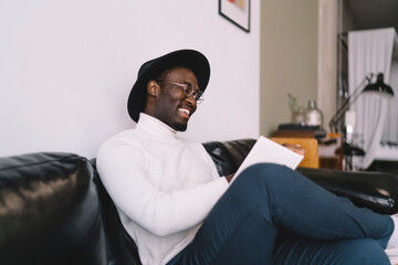 Happy black man reading textbook in living room