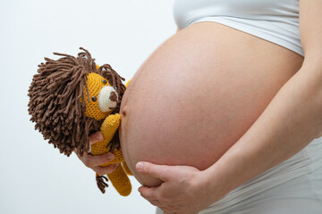 Close-up of a pregnant mother in whote cloths holding a stuffed lion and her hand on her bare round...
