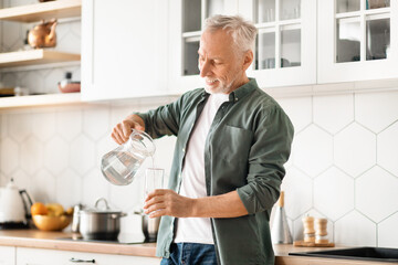 Happy elderly man filling his glass with water from jug in kitchen