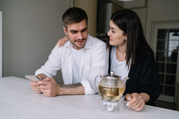 Happy couple using smartphone while sitting in kitchen