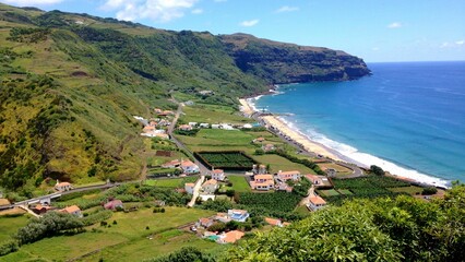 Fototapeta na wymiar View over the blue ocean and houses on the shore under mountains on a sunny day in Azores, Portugal