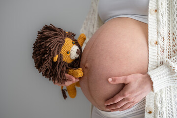 Close-up of a stuffed lion held by the mother's hand, who is looking excitedly at her naked, round belly and expecting the baby. Last month of pregnancy - week 39. White background. Bright shot.