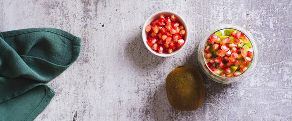 Tropical fruit kiwi, fresh yogurt and pomegranate seeds in a glass top view web banner