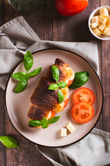 Baked caprese croissant with tomatoes, cheese and basil on a plate top and vertical view