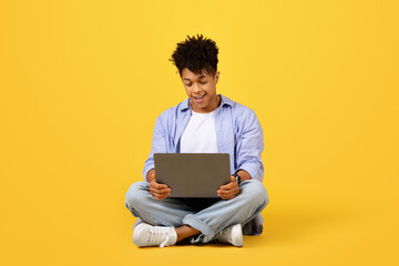 Black man using laptop on yellow background