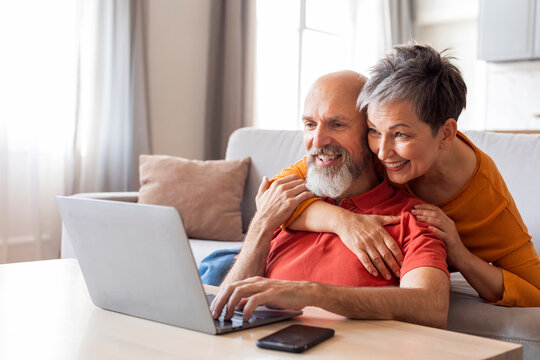 Smiling Senior Spouses Spending Time With Laptop In Living Room