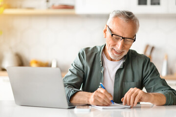 Online Learning For Older Adults. Senior Man Using Laptop And Taking Notes