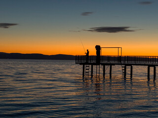 silhouette of the fisherman on the pier at sunset in the calm sea