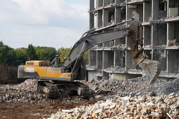 Fototapeta premium Building destruction, demolition of a building by an yellow excavator