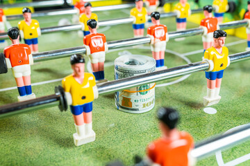 Table football game with roll of dollar bills in between plastic players, concept of betting and...