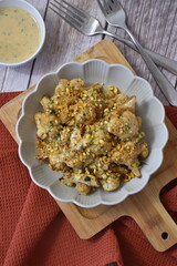Gray plate with food, cauliflower with sauce and peanuts with a wooden table background, board and red kitchen towel.