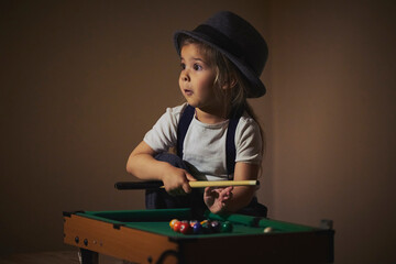 Charming child in retro clothes playing toy billiards