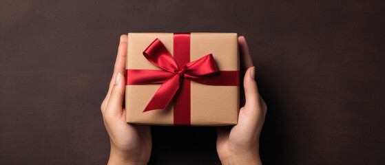 Female hands holding a gift box with a red bow on a wooden background.