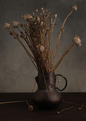 Still life with dried poppy bunch in old cracked brass jug vase.  Bouquet of dried flowers poppies...