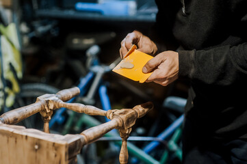 A man professional carpenter, woodworker coats a wooden chair with a plastic spatula with putty and...