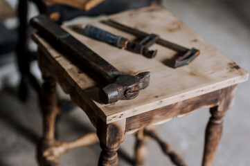 Locksmith tools, a hammer and a clamp lie on a wooden chair in the workshop. Photography, industry concept.