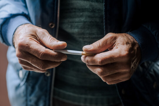 An elderly pensioner man is struggling with addiction, the desire to smoke, holding a cigarette in his hands. Medicine concept. Photography, close-up portrait.