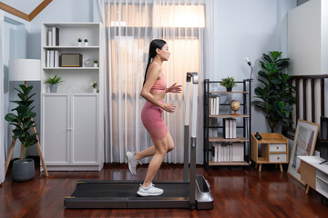 Full length side view of energetic and strong athletic asian woman running running machine at home. Pursuit of fit physique and commitment to healthy lifestyle with home workout and training. Vigorous - obrazy, fototapety, plakaty