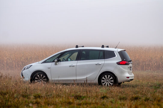 White family MPV car Opel Zafira stands on a field in the fog in autumn.