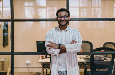 Fototapeta na wymiar Positive Hispanic man standing near wall of office