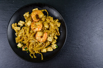 Black plate with pad thai on a slate board. Top view