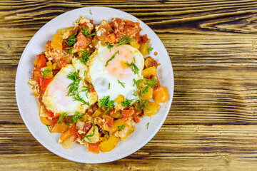 Homemade breakfast shakshuka with fried eggs, onion, bell pepper, tomatoes and dill on a wooden table. Jewish cuisine. Top view