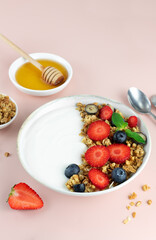 Yogurt bowl with granola and fresh berries: strawberries and blueberries on a pink background. Top view. 