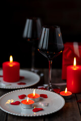 Saint Valentine's Day celebration. Red burning candles, hearts, gift box, postcard on dark wooden background. Happy holiday . Table decor for festive dinner, romantic atmosphere