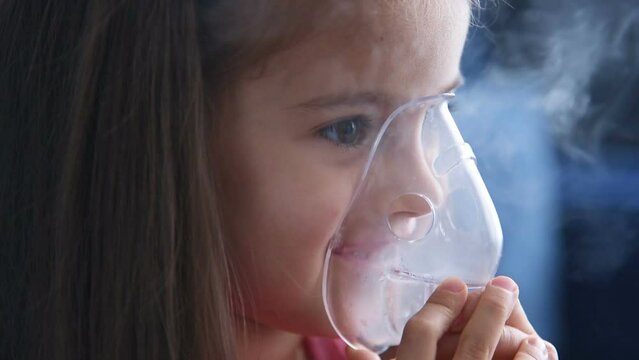 Happy little girl making inhalation with nebulizer. Child asthma nebulizer steam sick cough concept. Close up