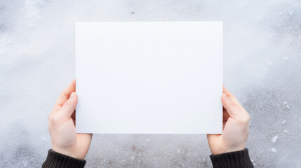 Top view of female hands holding blank paper sheet with copy space on snow background.