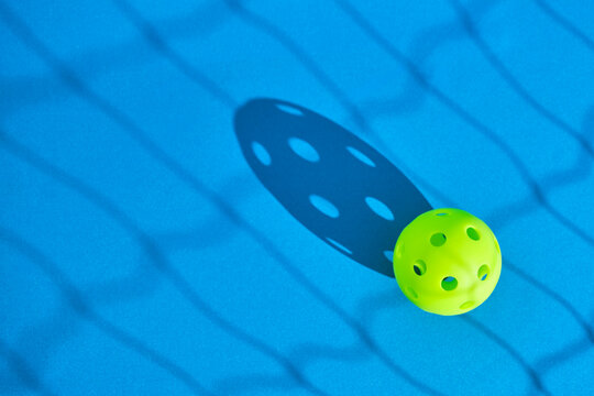 green pickleball ball on blue surface with the shadow of a net in front