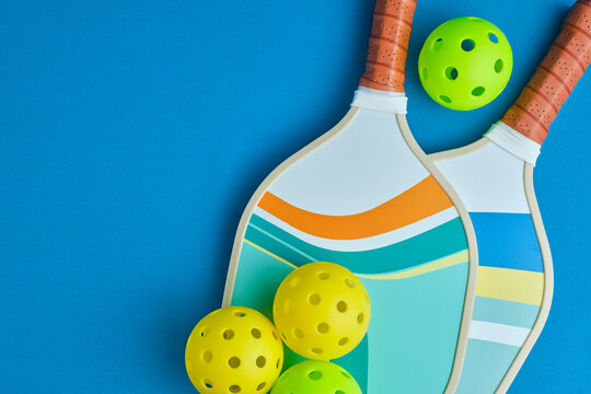 image from above of two pickleball paddles with three balls on a blue surface