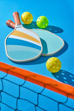 pickleball paddles with balls to the side on a blue background illuminated with hard light