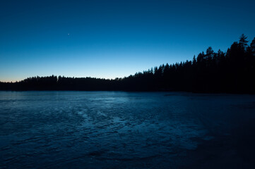 A small frozen lake in the forests of Finland in the blue light of evening