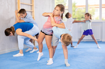 Obraz na płótnie Canvas Preteen children practicing in pair self-defence movements with female trainer supervision