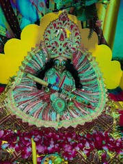Closeup shot of the idol of Laddu Gopal, sitting in a colorful dress, holding a flute