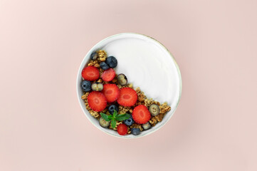 Yogurt bowl with granola and fresh berries: strawberries and blueberries on a pink background. Top view.
