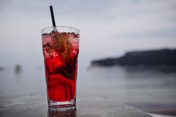 Fresh cold red color cocktail on the table by the sea with mountain view