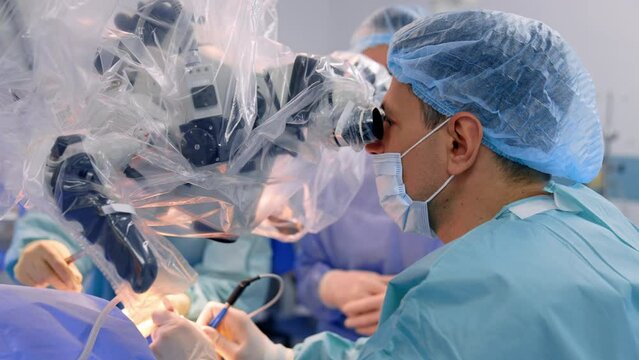 Attentive neurosurgeon performs microsurgery looking at microscope. Side view of a doctor carrying out neurosurgery.