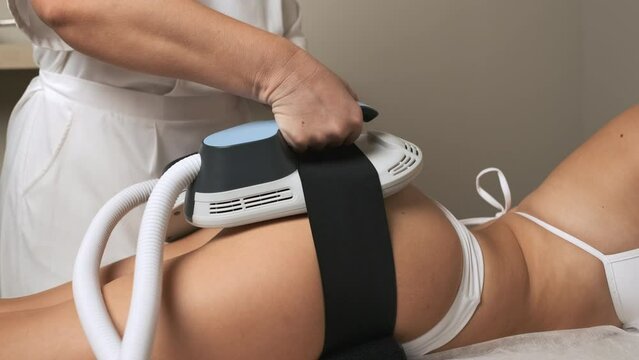 Female expert puts equipment on client buttocks in office. Procedure of body sculpting in medical institution. Caring for appearance of body part