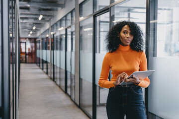Contemplative Black businesswoman with tablet in modern office passage, Her poised demeanor...